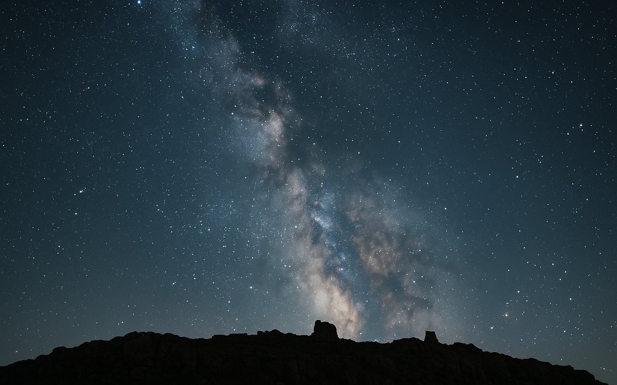 Night sky full of stars over the dark silhouette of Hadrian's Wall on the Whin Sill crags